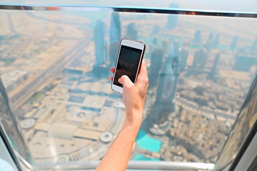 person-holding-mobile-phone-while-standing-by-window-city_1048944-8776590.jpg